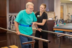 Therapist in black scrubs and blonde ponytail helping man in blue shirt
