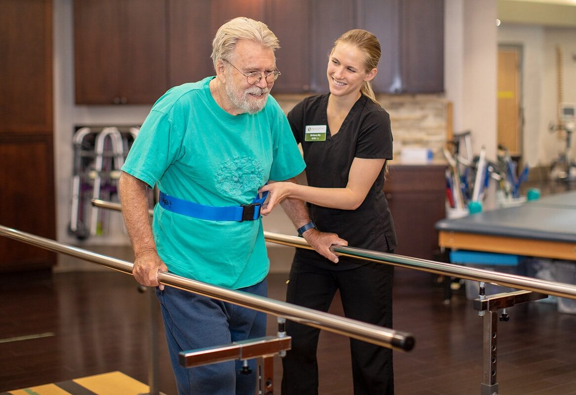 Therapist in black scrubs and blonde ponytail helping man in blue shirt