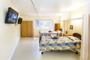 Double occupancy room with yellow and blue patchwork quilts on beds, and flat screen tv