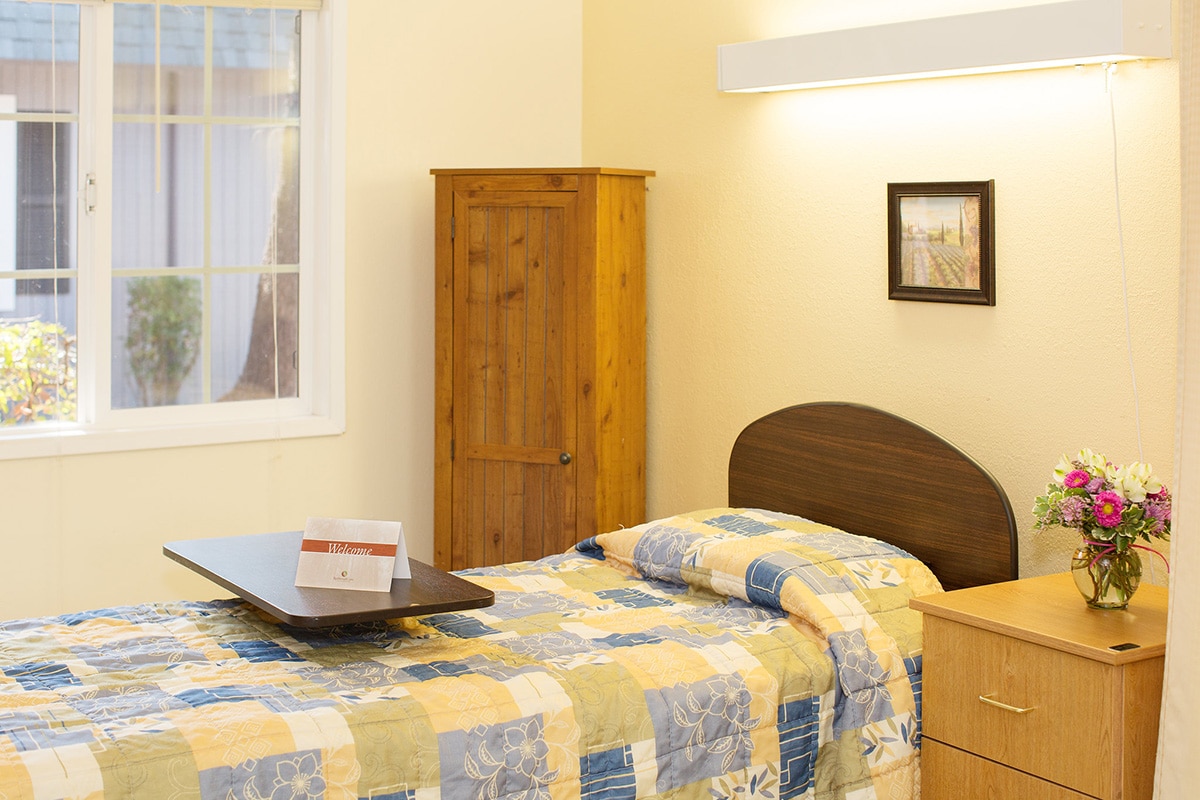 Patient room with yellow walls, pine cupboard, yellow and blue patchwork quilt.