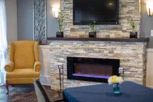 Close up of flagstone gas fireplace with yellow club chair next to it.