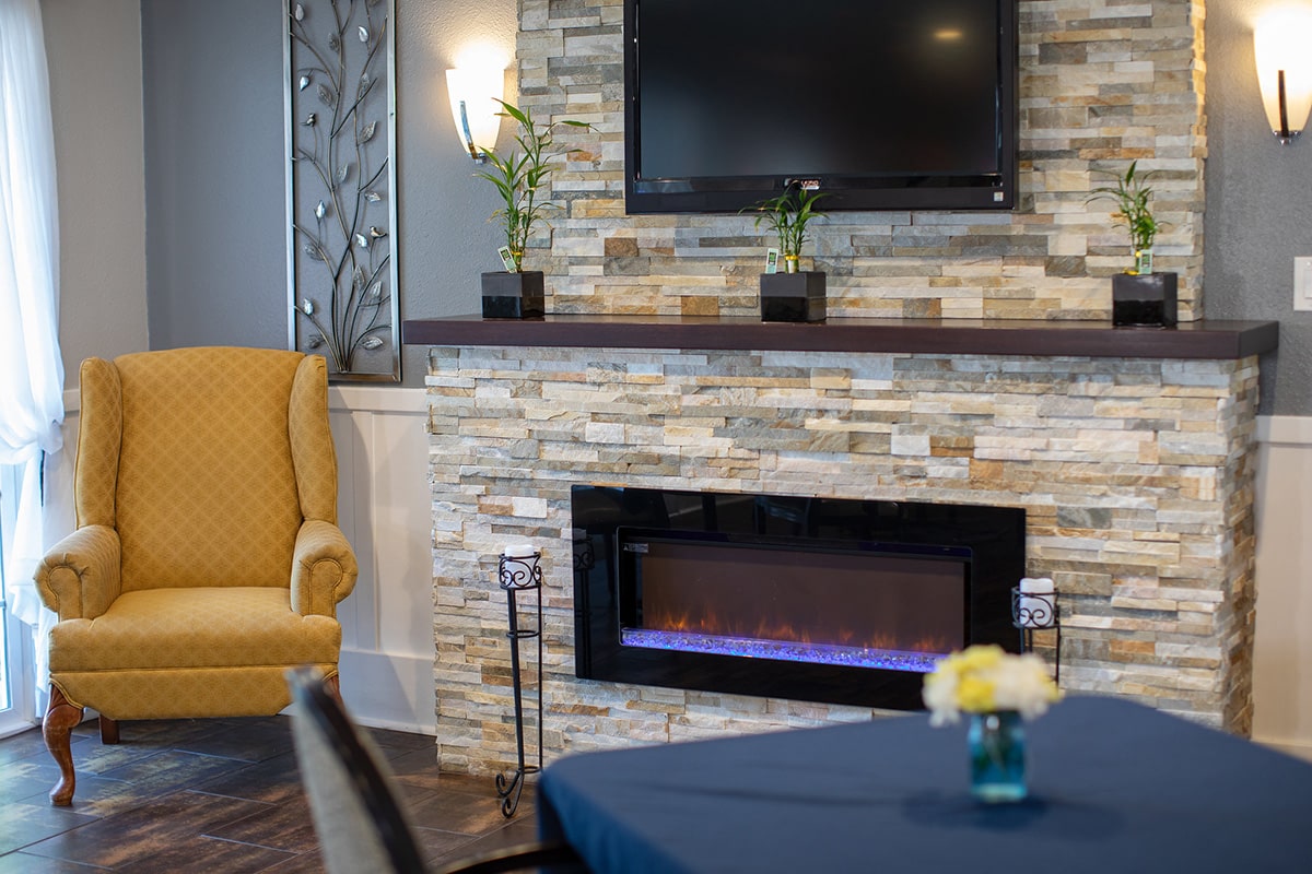 Close up of flagstone gas fireplace with yellow club chair next to it.