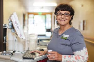 Medical professional working at a computer, smiling with glasses and brown hair.