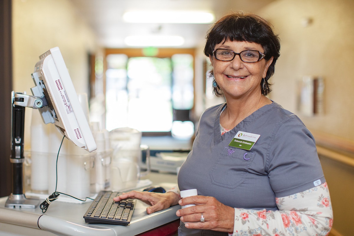 Medical professional working at a computer, smiling with glasses and brown hair.