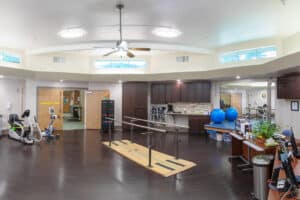 Larger shot of rehab gym with parallel bars, bikes, large bounce balls and other rehab equipment.