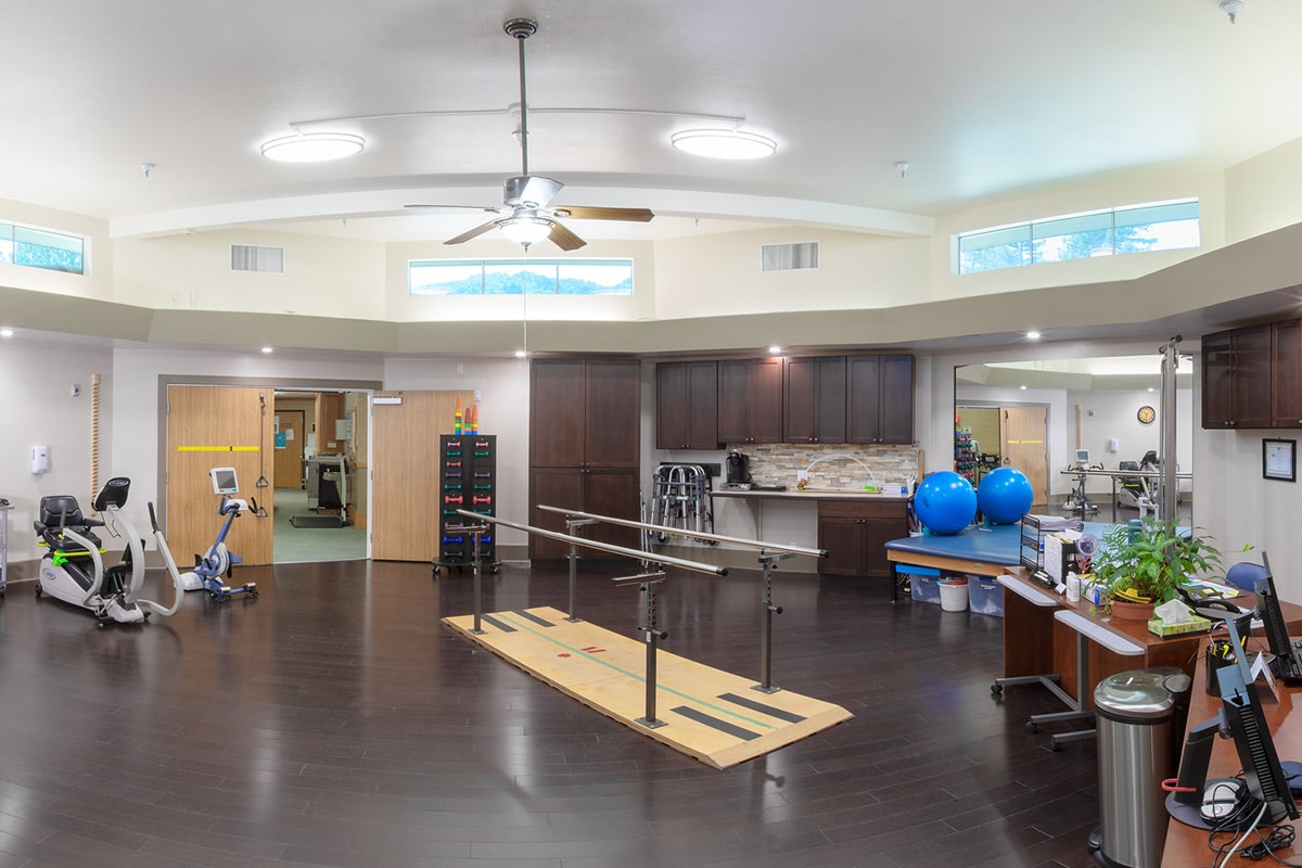 Larger shot of rehab gym with parallel bars, bikes, large bounce balls and other rehab equipment.