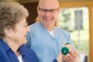 Therapist in blue scrubs helping woman with hand weights