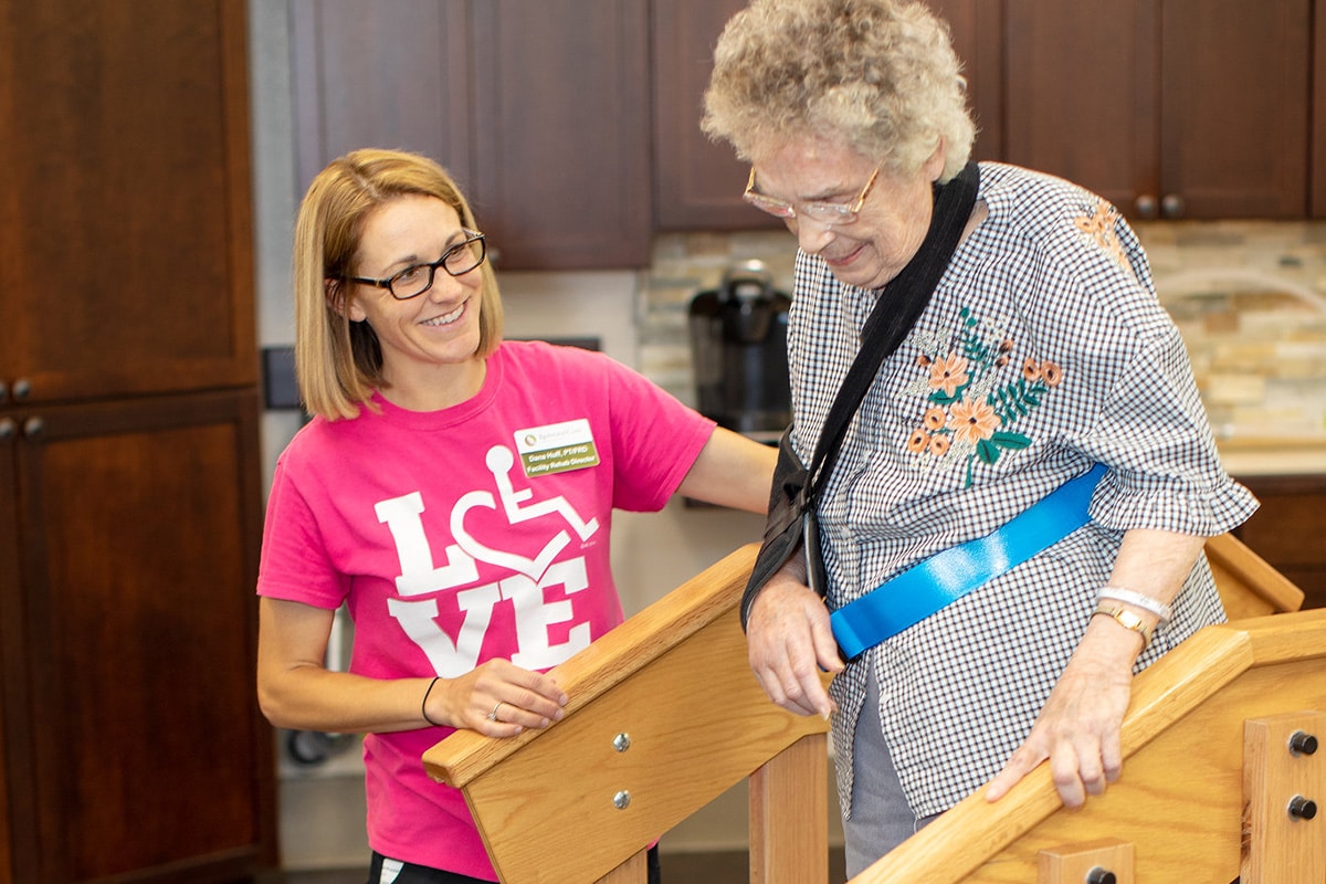 Therapist in pink shirt helping woman with sling on arm walk over rehab bridge