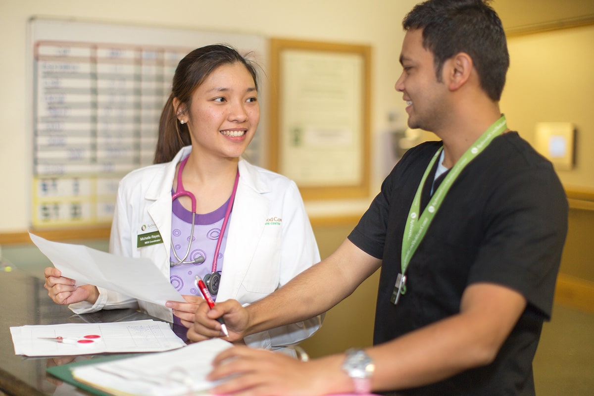 Two medical professionals in hallway looking at papers.