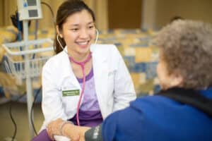 Medical professional in white lab coat smiling next to woman in blue shirt.