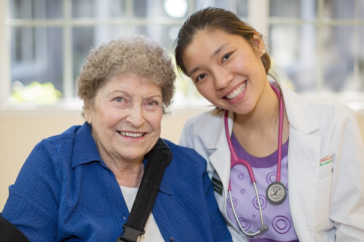 Medical professional in white lab coat smiling next to woman in blue shirt with curly hair.