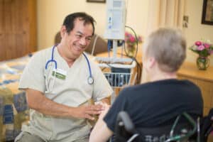Medical professional with stethoscope around his neck holding the hand of woman in wheelchair.