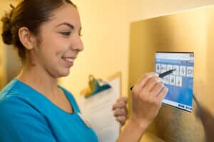 Medical professional in blue scrubs making notes in wall mounted computer.
